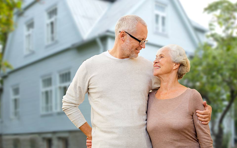 Happy senior couple hugging over house background